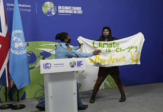 A member of security moves to apprehend a demonstrator at the COP26 U.N. Climate Summit in Glasgow, Scotland, Saturday, November 13, 2021. Almost 200 nations have accepted a contentious climate compromise aimed at keeping a key global warming target alive, but it contained a last-minute change that watered down crucial language about coal. (Photo by Alastair Grant/AP Photo)