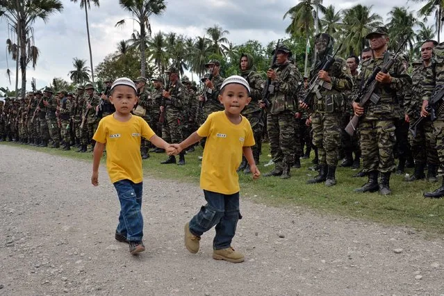 Two young boys walk past Moro Islamic Liberation Front (MILF) rebels, lined up in formation, during a rally in support of the peace signing agreement at Camp Darapanan in the town of Sultan Kudarat on the southern Philippine island of Mindanao on March 27, 2014. The biggest Muslim rebel group in the Philippines signed an historic pact on March 27 to end one of Asia's longest and deadliest conflicts, promising to give up their arms for an autonomous homeland. (Photo by Ted Aljibe/AFP Photo)
