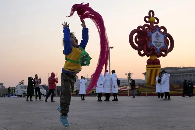 A child plays with a red scarf near a decoration for the Beijing Winter Olympics on Tiananmen Square in Beijing, China, Tuesday, January 18, 2022. (Photo by Ng Han Guan/AP Photo)