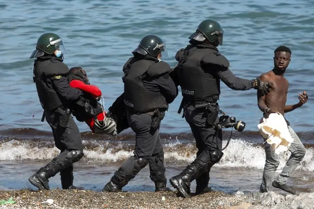 Spanish security forces members carry and escort Moroccan citizens at El Tarajal beach, near the fence between the Spanish-Moroccan border, after thousands of migrants swam across this border during last days, in Ceuta, Spain, May 18, 2021. Ceuta, a Spanish city of 85,000 in northern Africa, faces a humanitarian crisis after thousands of Moroccans took advantage of relaxed border control in their country to swim or paddle in inflatable boats into European soil. (Photo by Jon Nazca/Reuters)