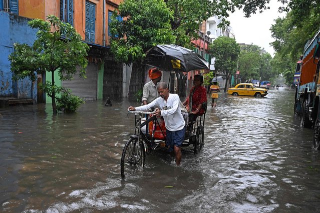 People move through a waterlogged street during rainfall in Kolkata on May 27, 2024, following the landfall of Cyclone Remal in India's West Bengal state. Residents of low-lying areas of Bangladesh and India surveyed the damage on May 27 as an intense cyclone that lashed the coast weakened into a heavy storm after killing at least three people, damaging homes and uprooting trees. (Photo by Dibyangshu Sarkar/AFP Photo)