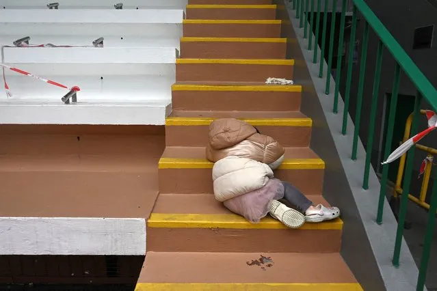 A child sleeps on steps while waiting with her mother for a Covid-19 test at a sports ground in Hong Kong on February 23, 2022, as the city faces its worst coronavirus wave to date. (Photo by Peter Parks/AFP Photo)