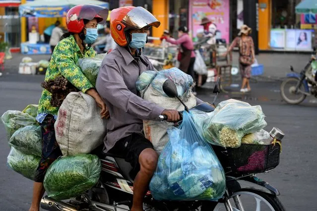 A couple transport vegetables on a motorcycle in Phnom Penh on March 8, 2022. (Photo by Tang Chhin Sothy/AFP Photo)