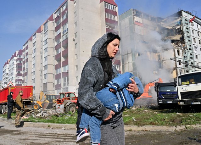 A woman walks past damaged residential buildings as she carries a child in Kyiv on April 28, 2023, after Russian missile strikes targeted several Ukrainian cities overnight. Ukraine and Russia have been fighting since Moscow's February 2022 invasion and Ukraine says it has been preparing for months a counter-offensive aimed at repelling Russian forces from the territory they currently hold in the east and south. (Photo by Sergei Supinsky/AFP Photo)