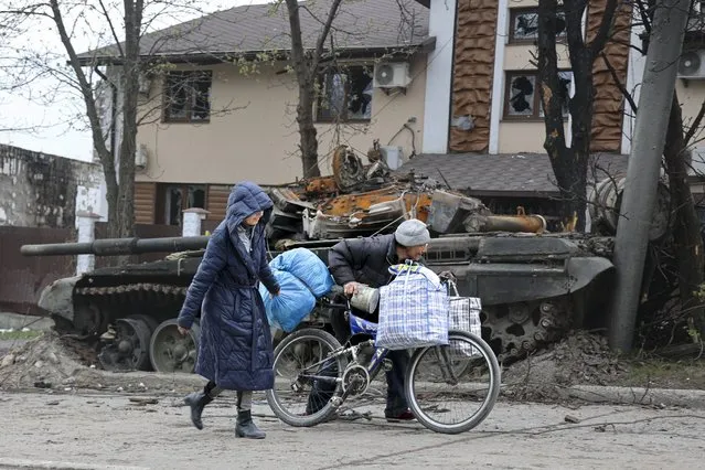 Local civilians walk past a tank destroyed during heavy fighting in an area controlled by Russian-backed separatist forces in Mariupol, Ukraine, Tuesday, April 19, 2022. (Photo by Alexei Alexandrov/AP Photo)