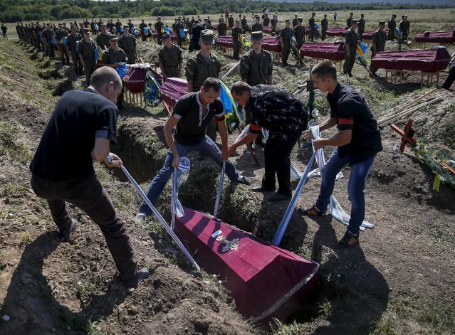 Workers take part in a mass funeral ceremony to bury 57 unidentified members of Ukrainian military forces who were killed in the conflict in eastern regions, in the settlement of Kushuhum near Zaporizhia, Ukraine, August 7, 2015. (Photo by Gleb Garanich/Reuters)