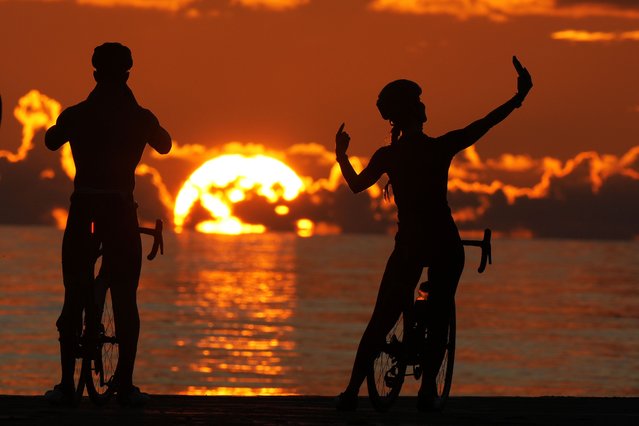 A pair of cyclists take photos as the sun rises over the Atlantic Ocean, Thursday, October 3, 2024, in Bal Harbour, Fla. (Photo by Wilfredo Lee/AP Photo)