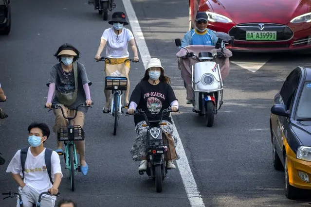 People wearing face masks ride bicycles and scooters along a street in Beijing, Friday, July 8, 2022. (Photo by Mark Schiefelbein/AP Photo)