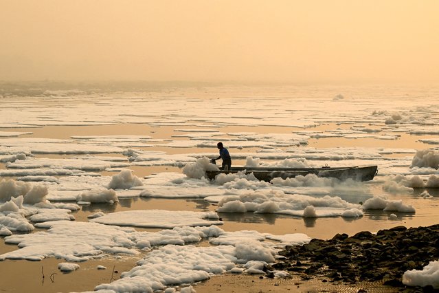 A man steers his boat across river Yamuna laden with toxic foam, as smog engulfs New Delhi on November 6, 2024. (Photo by Money Sharma/AFP Photo)