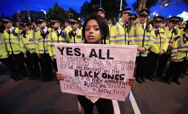 Police form a cordon on Brixton Road, as a demonstrator holds up a poster during a protest against the killing of two black men in the United States, in London, Saturday July 9, 2016. It followed a protest in central London on Friday after the shooting of black men by US police in Baton Rouge, Louisiana, and St Paul, Minnesota. Those deaths were followed by the reprisal shooting of five officers in Dallas, Texas. (Photo by Jonathan Brady/PA Wire via AP Photo)