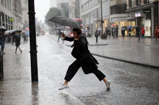 A pedestrian leaps over a puddle as rain fell in central London on August 9, 2017. (Photo by Tolga Akmen/AFP Photo)