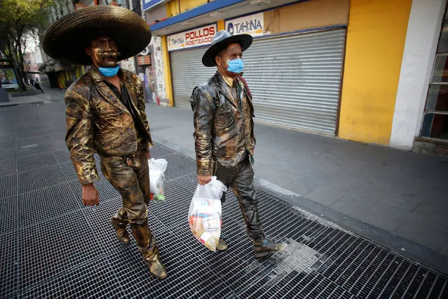 Street performers dressed as statues, wearing protective face masks, carry food handed over by an organization to help them due to the lack of work following the measures issued by Mexico's government for the health emergency to curb the spread of the coronavirus disease (COVID-19), in Mexico City, Mexico on April 16, 2020. (Photo by Gustavo Graf/Reuters)