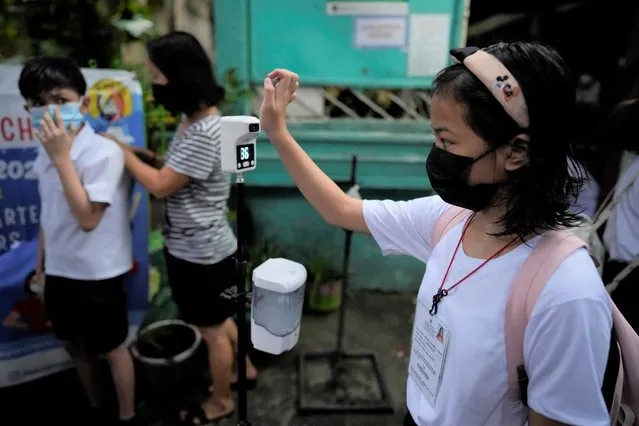 A student checks her temperature during the opening of classes at the San Juan Elementary School in metro Manila, Philippines on Monday, August 22, 2022. Millions of students wearing face masks streamed back to grade and high schools across the Philippines Monday in their first in-person classes after two years of coronavirus lockdowns that are feared to have worsened one of the world's most alarming illiteracy rates among children. (Photo by Aaron Favila/AP Photo)