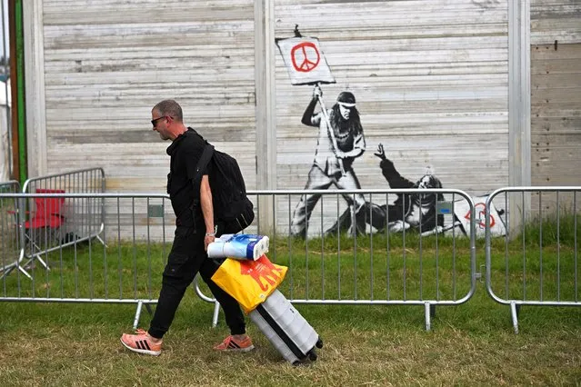 Revellers walk by a graffiti attributed to Banksy as they arrive at Worthy Farm in Somerset during the Glastonbury Festival in Britain, June 23, 2022. (Photo by Dylan Martinez/Reuters)