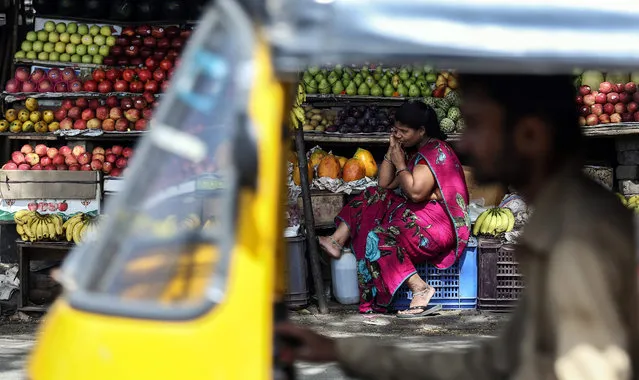 A fruit vendor talks on her mobile phone as a man drives past in a tuk tuk, at a market in Mumbai, India, 03 September 2015. (Photo by Divyakant Solanki/EPA)