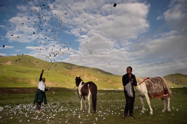 In this picture taken on July 26, 2016 Tibetan nomad horseman throw papers leafs with prayers written on them as high as they can next to their horse for good luck ahead of a horse race on the Tibetan Plateau in Yushu County. Set between emerald hills on the Himalayan plateau, some 3,700 metres above sea level, Yushu's annual equine festival is billed as a showcase of Chinese government support for Tibetan culture. (Photo by Nicolas Asfouri/AFP Photo)