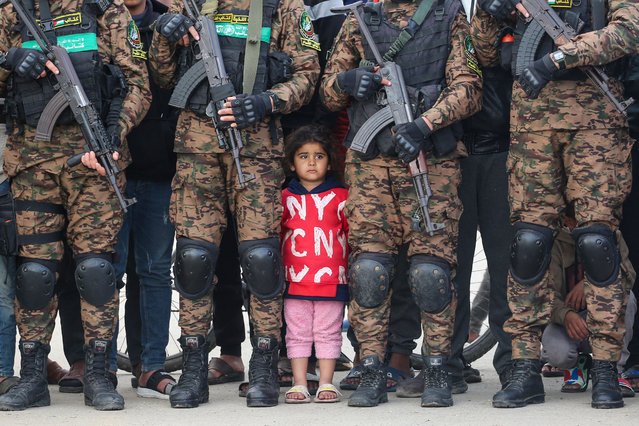 A Palestinian girl stands between Hamas fighters as she watches the handover of three Israeli hostages to a Red Cross team in Deir el-Balah, central Gaza, on February 8, 2025. Hamas militants handed over three Israeli hostages on February 8, as part of the fifth exchange under a fragile Gaza ceasefire, with 183 prisoners held by Israel due to be released later in the day. (Photo by Eyad Baba/AFP Photo)
