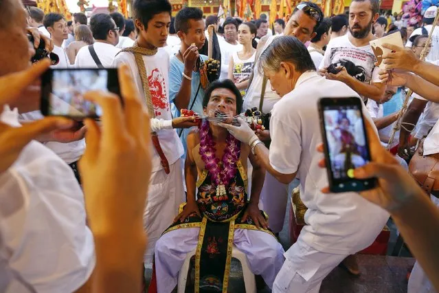 People take pictures as a devotee of the Chinese Bang Neow Shrine is helped to insert more spikes through his cheeks before a procession celebrating the annual vegetarian festival in Phuket September 29, 2014. (Photo by Damir Sagolj/Reuters)