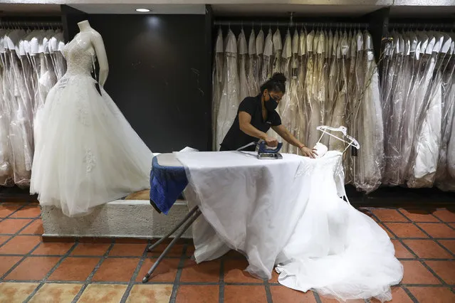 A woman wearing a mask to curb the spread of the new coronavirus irons a wedding dress at a store in Mexico City, Tuesday, June 30, 2020. (Photo by Eduardo Verdugo/AP Photo)