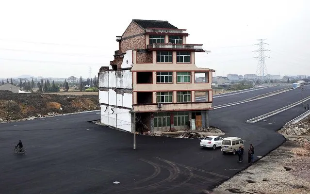People stand near a house which sits in the middle of a newly built road in Wenling city in east China's Zhejiang province November 22, 2012. The house belongs to an elderly man, who refused to sign an agreement to allow his house to be demolished by the authorities, as the compensation offered to him was not enough, according to local media. (Photo by AFP Photo/Associated Press)