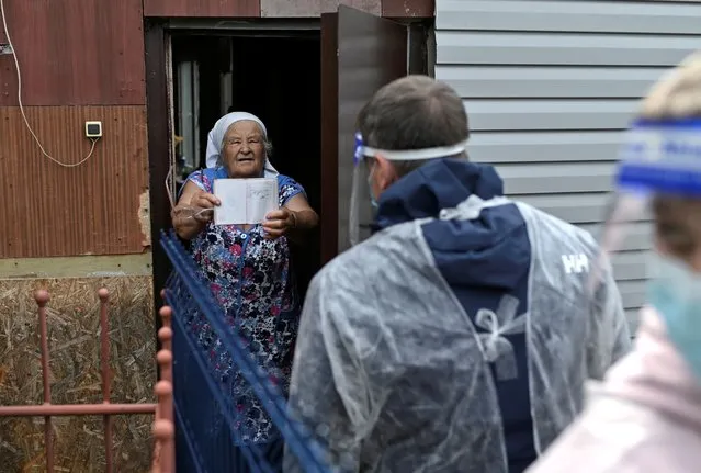 An elderly woman shows her passport to members of an electoral commission wearing a protective face mask and shield, used as a preventive measure against the spread of the coronavirus disease (COVID-19), who visit local residents during a seven-day nationwide vote on constitutional reforms in the village of Nikolayevka in Omsk Region, Russia on June 26, 2020. (Photo by Alexey Malgavko/Reuters)