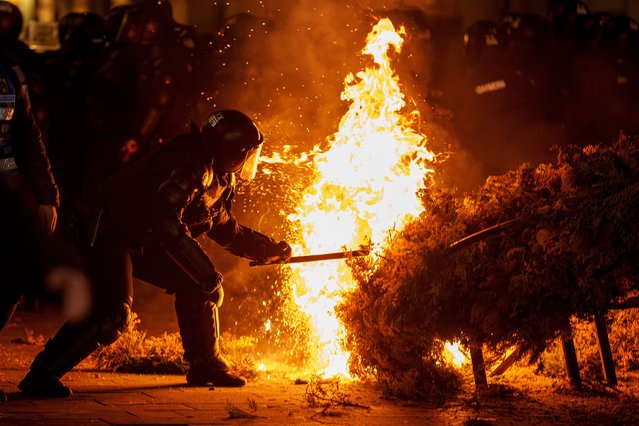 A riot policeman attempts to extinguish a fire as supporters of Calin Georgescu protested the electoral body's decision to reject his candidacy in a presidential election redo in Bucharest, Romania, Sunday, March 9, 2025. (Photo by Vadim Ghirda/AP Photo)