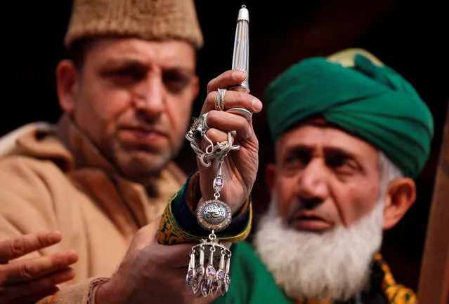 A Kashmiri Muslim cleric (wearing green turban) displays a relic (inside glass tube) of Sheikh Abdul Qadir Jeelani, a Sufi saint, also known as Shah-e-Baghdad (King of Baghdad), on Jeelani's death anniversary in Srinagar December 30, 2017. (Photo by Danish Ismail/Reuters)