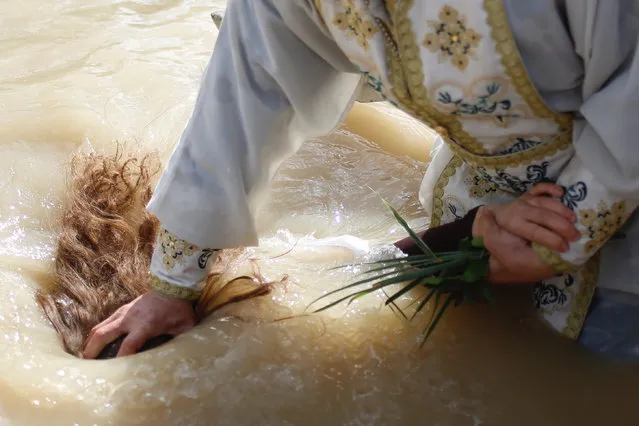 A Christian Orthodox priest re-enacts the baptism of Jesus, during the traditional Epiphany baptism ceremony at the Qasr-el Yahud baptism site, in the Jordan river near the West Bank town of Jericho, Thursday, January 18, 2018. (Photo by Ariel Schalit/AP Photo)