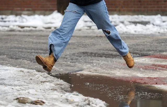 A person leaps over a puddle of water and slush as rain falls in Montreal, Friday, December 23, 2022, as a storm system bears down on the region. (Photo by Graham Hughes/The Canadian Press via AP Photo)