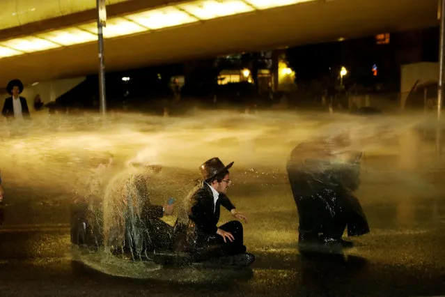 Israeli ultra-Orthodox Jewish men sit as a water canon is activated during a protest against the detention of a member of their community who refuses to serve in the Israeli army, in Jerusalem March 8, 2018. (Photo by Ronen Zvulun/Reuters)
