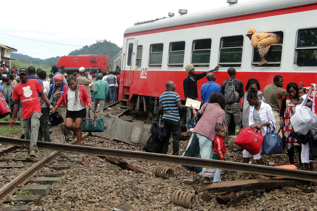 A passenger escapes a train car using a window as others leave from the site of a train derailment in Eseka on October 21, 2016. Fifty-three were killed and over 300 injured when a packed Cameroon passenger train derailed on October 21 while travelling between the capital Yaounde and the economic hub Douala, state broadcaster Crtv said. The train, crammed with people due to road traffic disruption between the two cities, left the tracks just before reaching the central city of Eseka, Transport minister Edgar Alain Mebe Ngo'o said earlier. (Photo by AFP Photo/Stringer)