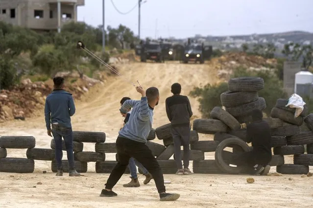 A Palestinian demonstrator hurls stone toward Israeli soldiers to protest a march by Israeli settlers, in the West Bank village of Beita, Monday, April 10, 2023. Thousands of settlers marched to Eviatar, an unauthorized settlement outpost located next to Beita in the northern West Bank. (Photo by Majdi Mohammed/AP Photo)