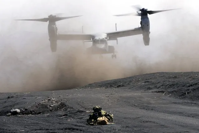 An MV-22 Osprey takes off as one of members of the Japan Ground Self-Defense Force (JGSDF) guards the landing zone during a joint military helicopter borne operation drill between JGSDF and U.S. Marines at the Higashi Fuji range in Gotemba, southwest of Tokyo, Tuesday, March 15, 2022. (Photo by Eugene Hoshiko/AP Photo)