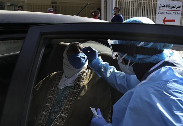 A nurse in protective clothing takes a swab from a woman in her car near the emergency entrance of a coronavirus testing center in the Rafik Hariri University Hospital in Beirut, Lebanon, Monday, January 11, 2021. Lebanon's caretaker prime minister said Monday the country has entered a “very critical zone” in the battle against coronavirus as his government mulls tightening nationwide lockdown announced last week. (Photo by Bilal Hussein/AP Photo)
