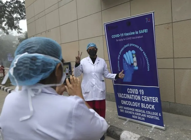 A health worker gestures as she gets her photograph taken next to a COVID-19 vaccination banner at a hospital in New Delhi, India, Saturday, January 16, 2021. India started inoculating health workers Saturday in what is likely the world's largest COVID-19 vaccination campaign, joining the ranks of wealthier nations where the effort is already well underway. (Photo by Manish Swarup/AP Photo)