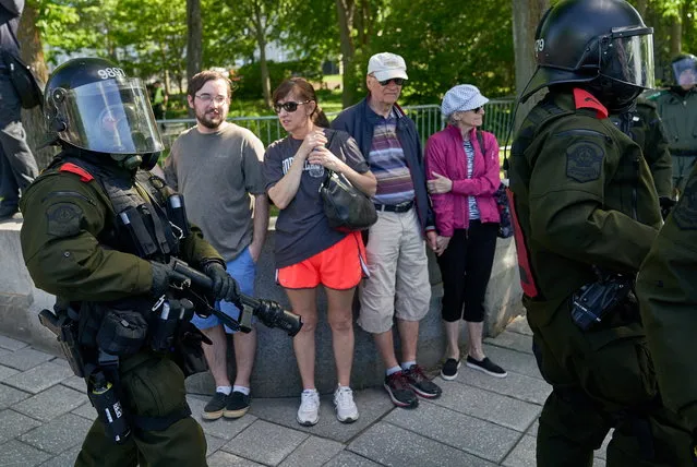 Tourists look at anti riot police passing by during a protest against the G7 Summit in Quebec City, Quebec, Canada, 09 June 2018. Leaders of the US, Canada, France, Germany, Japan, Italy, the United Kingdom as well as the European Union will gather in Le Manoir Richelieu in La Malbaie for the two day summit on 08 June and 09 June 2018. (Photo by Andre Pichette/EPA/EFE)