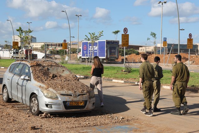 Israeli soldiers and a woman walk past a damaged vehicle in the aftermath of an Iranian missile attack on Israel, on October 2, 2024 in Tel Aviv. Israel vowed to make Iran “pay” for firing a barrage of missiles at its territory, with Tehran warning on October 2 it would launch an even bigger attack it is targeted. (Photo by Jack Guez/AFP Photo)