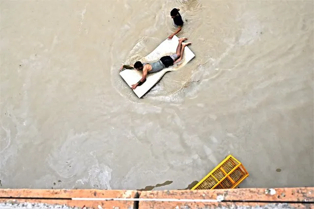 A man floats on thermacol through a flooded street after Yamuna River overflowed due to monsoon rains in New Delhi on July 14, 2023. (Photo by Arun Sankar/AFP Photo)