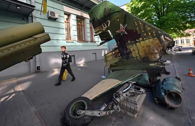 A pedestrian passes in front of the wreckage of a Russian plane outside the National Museum of Military History of Ukraine in Kyiv on May 5, 2022. The exhibit's curator Pavlo Netesov hopes the freshly destroyed equipment will serve as a visible reminder of the war's toll to residents in downtown Kyiv – who have been largely spared from the harsh ground fighting that has erupted elsewhere across the country. (Photo by Sergei Supinsky/AFP Photo)