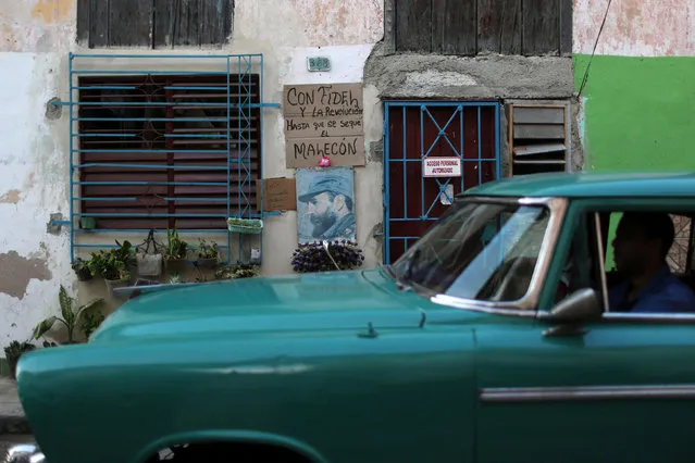 A man drives a vintage car as he passes by an image of Fidel Castro in downtown Havana, Cuba, November 27, 2016. The sign reads: “With Fidel and the Revolution until the Malecon gets dry”. (Photo by Alexandre Meneghini/Reuters)