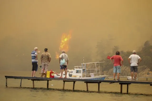 Tourists wait to be evacuated from smoke-engulfed Mazi area as wildfires rolled down the hill toward the seashore, in Bodrum, Mugla, Turkey, Sunday, August 1, 2021. More than 100 wildfires have been brought under control in Turkey, according to officials. The forestry minister tweeted that five fires are continuing in the tourist destinations of Antalya and Mugla. (Photo by Emre Tazegul/AP Photo)