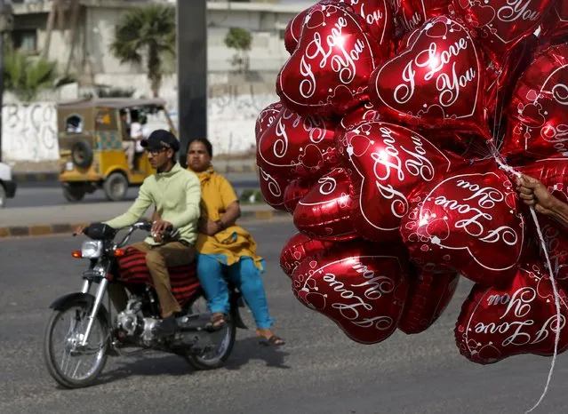 A couple on a motorcycle ride past a vendor selling heart-shaped balloons on Valentine's Day in Karachi, Pakistan February 14, 2016. (Photo by Akhtar Soomro/Reuters)