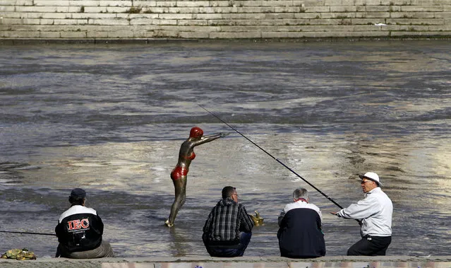 Men talk to each other while fishing by a sculpture set in the Vardar River, in Skopje, Macedonia, Friday, February 19, 2016. Periods of sun and rain with unusually high temperatures for this time of the year of up to 20 degrees Celsius (68 Fahrenheit), is expected over the next few days in the Balkan country. (Photo by Boris Grdanoski/AP Photo)