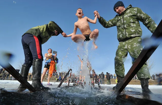 Cossacks help a boy to take a bath in the icy waters of a lake during the celebration of the Epiphany holiday near the village of Leninskoe, some 15 km of Bishkek, on January 19, 2017. (Photo by Vyacheslav Oseledko/AFP Photo)