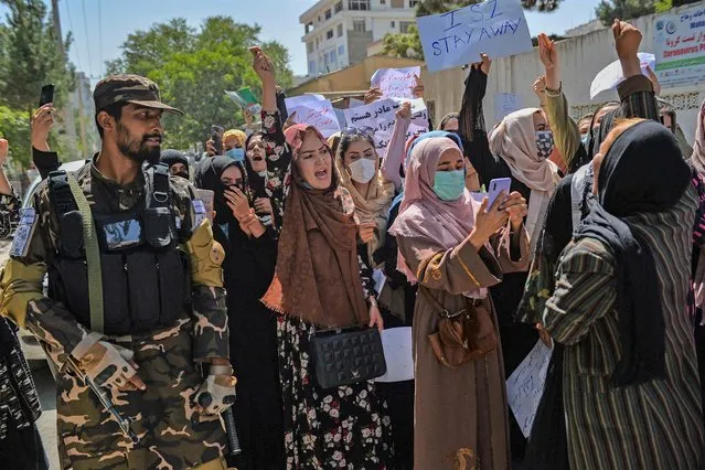 A Taliban fighter stands guard as Afghan women shout slogans during an anti-Pakistan protest rally, near the Pakistan embassy in Kabul on September 7, 2021. The Taliban on September 7, 2021 fired shots into the air to disperse crowds who had gathered for an anti-Pakistan rally in the capital, the latest protest since the hardline Islamist movement swept to power last month. (Photo by Hoshang Hashimi/AFP Photo)