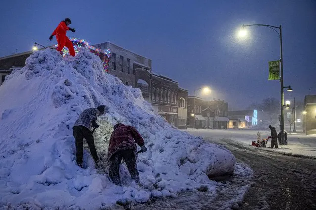 People stand on a large snow pile in Oskaloosa, Iowa, Tuesday, January 9, 2024, as another person uses a snow blower.(Photo by Andrew Harnik/AP Photo)