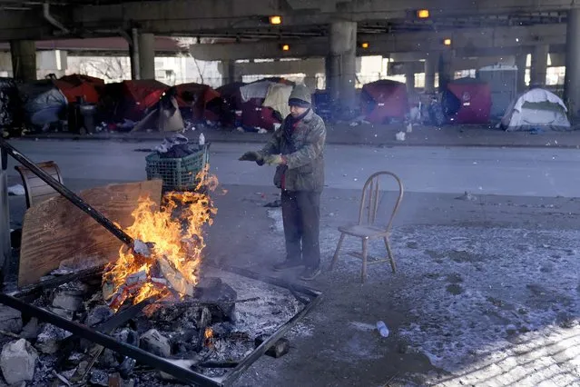An elderly man warms his hands by the fire he created across the street from a homeless encampment under a major interstate freeway Tuesday, January 16, 2024, in Chicago. Millions of Americans face below-zero temperatures as storms bring a blast of Arctic air, snow and ice. (Photo by Charles Rex Arbogast/AP Photo)