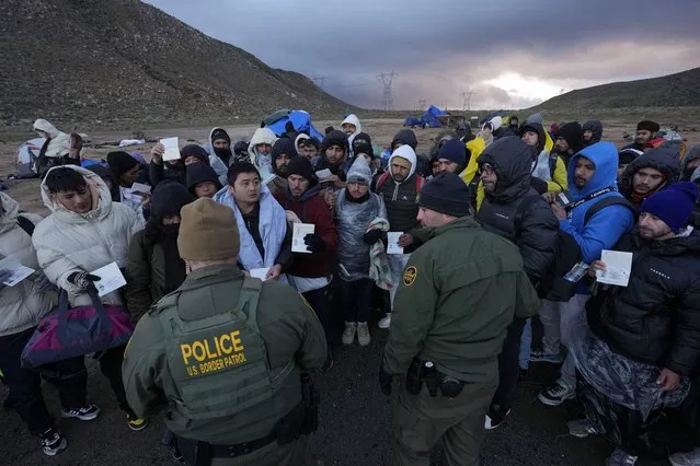 U.S. Border Patrol agents, front, speak with migrants seeking asylum, mainly from Colombia, China and Ecuador, in a makeshift, mountainous campsite after crossing the border between Mexico and the United States, Friday, February 2, 2024, near Jacumba, Calif. About 200 migrants huddled under blankets and plastic bags under pounding rain and wind Friday night, as Border Patrol agents tried to work out transportation to area facilities. (Photo by Gregory Bull/AP Photo)