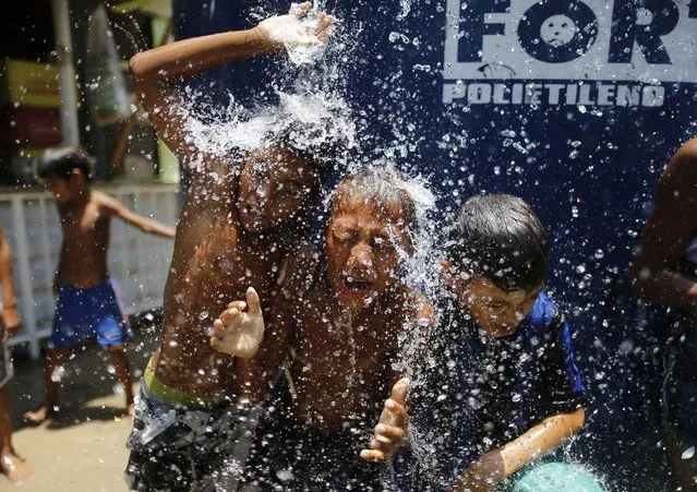 In this January 29, 2015 file photo, children play under the water that they manage to spill over from a water tank, to cool off from the summer heat, at the Alemao Complex slum in Rio de Janeiro, Brazil. (Photo by Leo Correa/AP Photo)