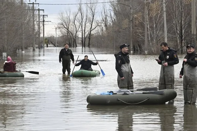 Police officers stand guarding an area as people use rubber boats in a flooded street after part of a dam burst, in Orsk, Russia on April 7, 2024. (Photo by Anatoly Zhdanov/Kommersant Publishing House via AP Photo)